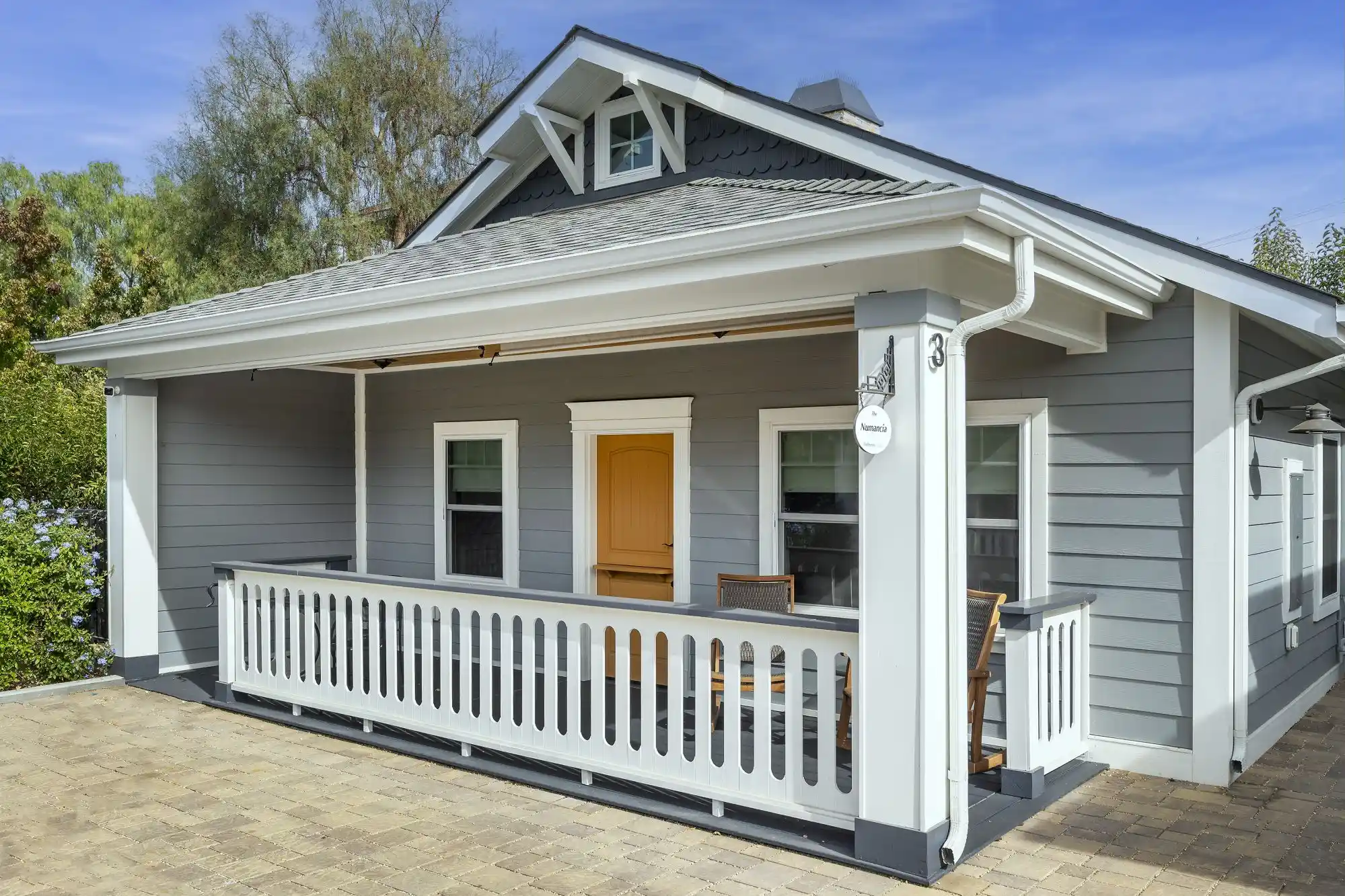 Small white house with a front porch and an orange door.